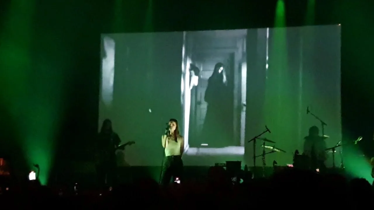 Ethel Cain in a long black dress with the band around her, the Roundhouse lit deep blue. The Roundhouse, London · 10 June 2024. Frame from footage by inklungs, © the uploader.