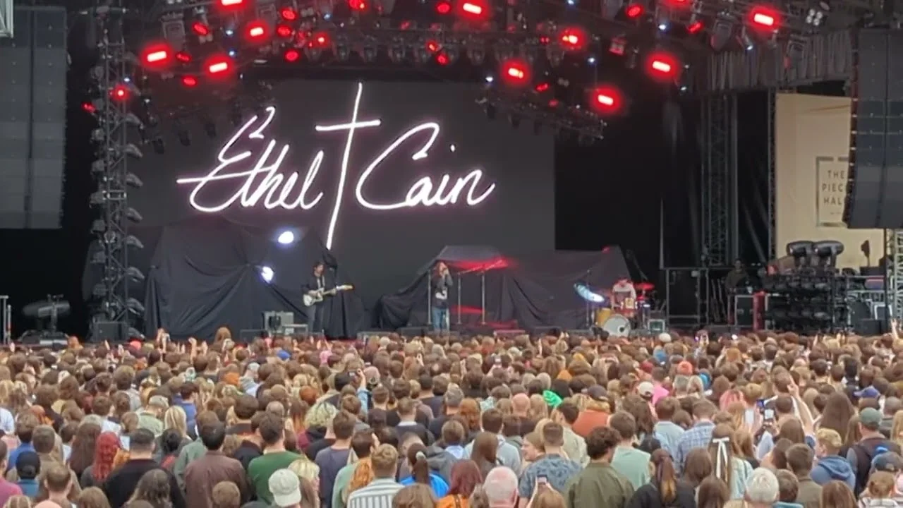 The Ethel Cain script banner lit above an open-air stage, the crowd packed to the back of the square. The Piece Hall, Halifax · 23 August 2023. Frame from footage by Sam Wilkie, © the uploader.