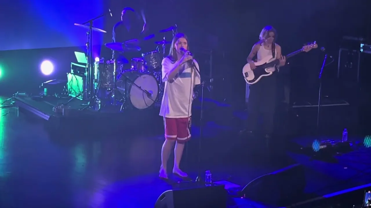Ethel Cain close on the microphone, the whole room behind her washed hard green. Le Trianon, Paris · 2024. Frame from footage by Nocx, © the uploader.