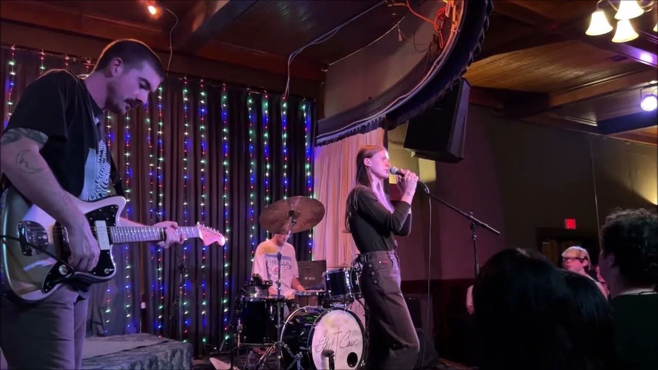 Ethel Cain and her band on the floor of a small wood-panelled hall, the guitarist nearest the camera, drums behind. Sons of Hermann Hall, Dallas · 2 September 2022. Frame from footage by Daniel Kirby, © the uploader.